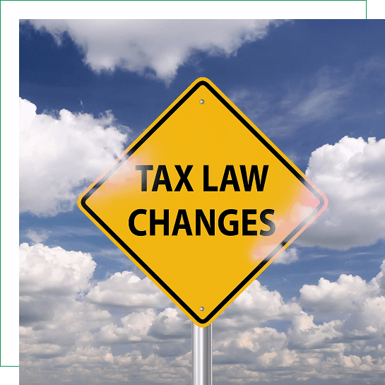 Yellow road sign warning about tax law changes against a cloudy sky.